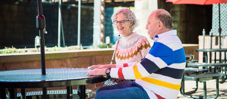 Two blind seniors chat together at an outdoor table.
