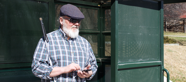A man stands at a bus stop listening to his phone.
